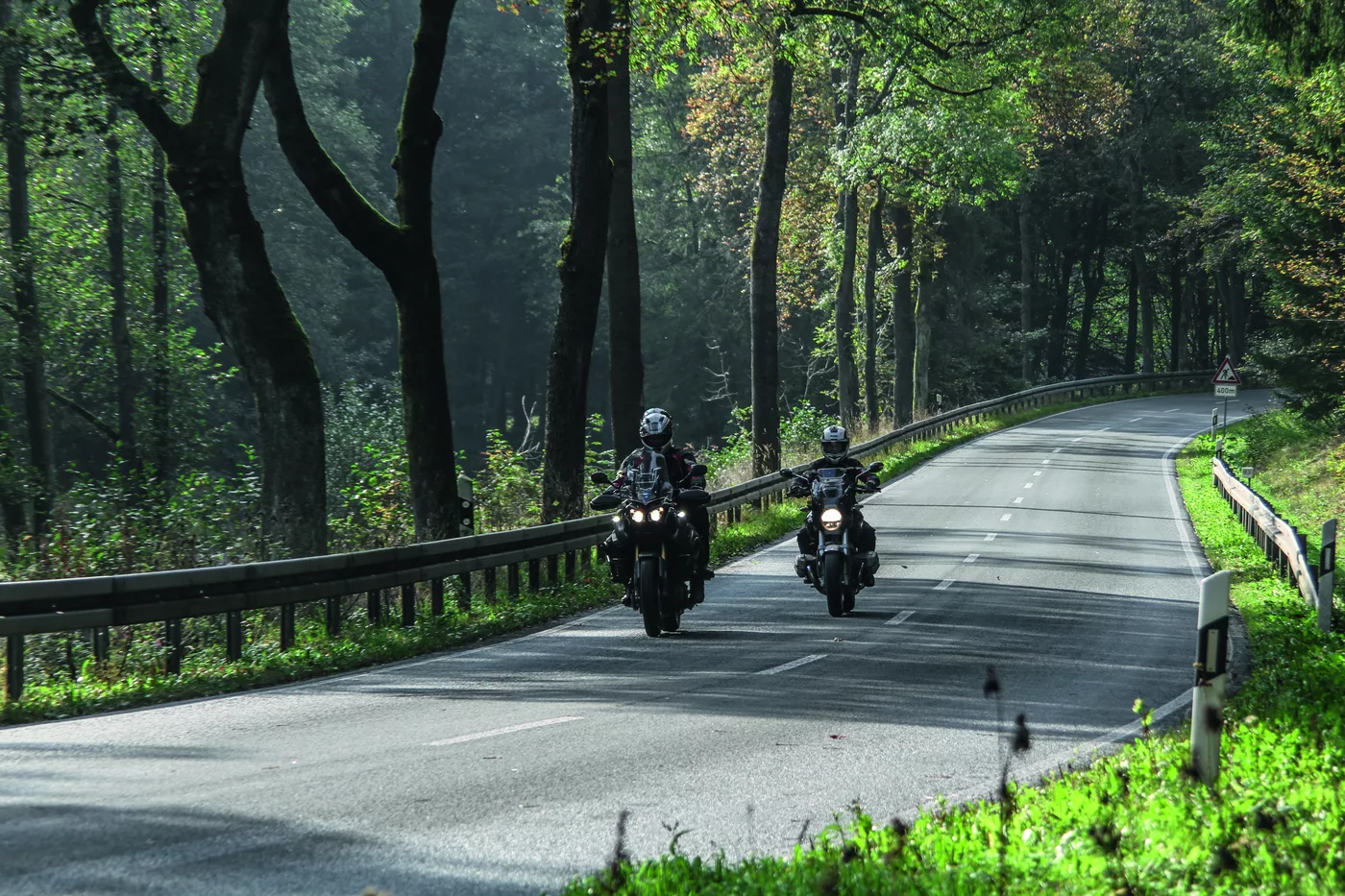Zwei Motorräder auf einer von Bäumen gesäumten Straße am Morgen Zwei Motorräder auf einer von Bäumen gesäumten Straße am Morgen